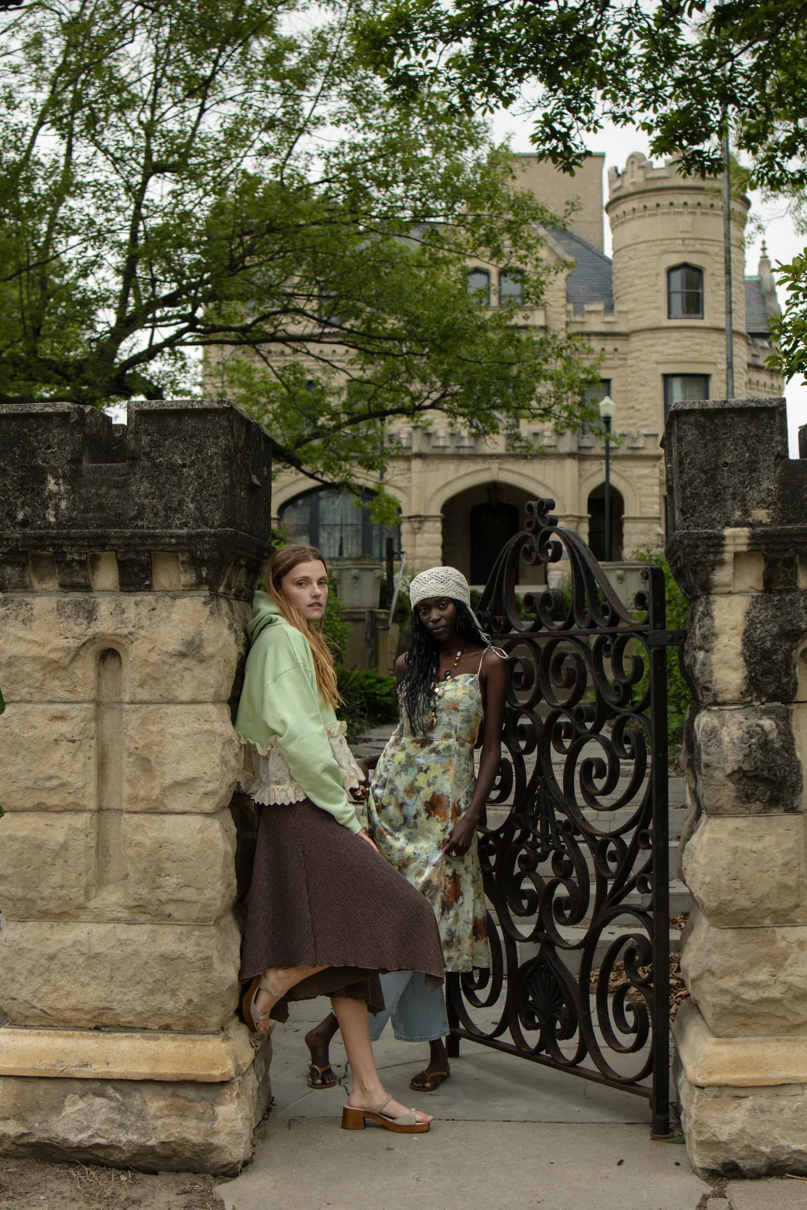 Two women pass through an iron gate below a stone castle.