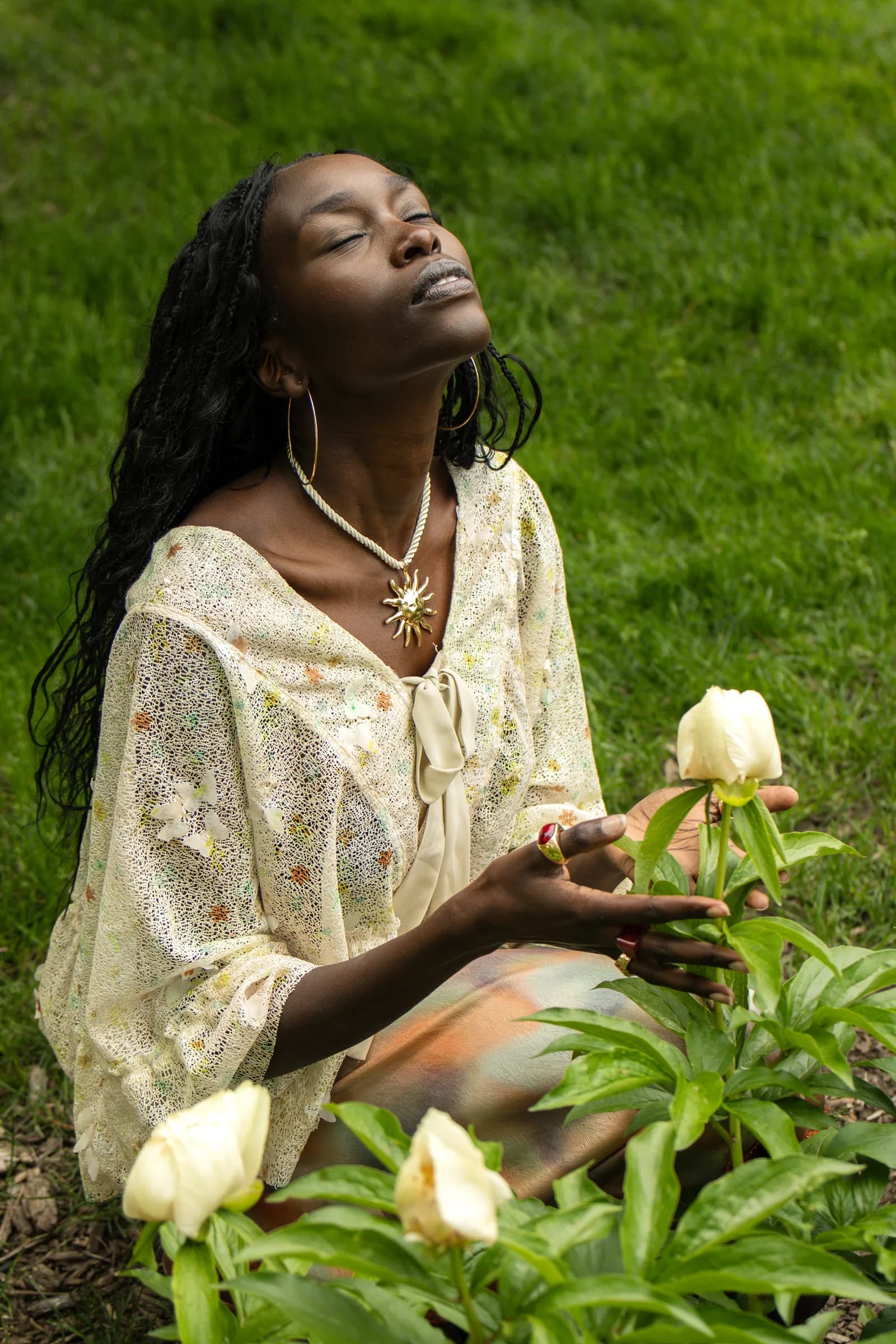 A woman in a cream lace blouse closes her eyes beside a white peony.