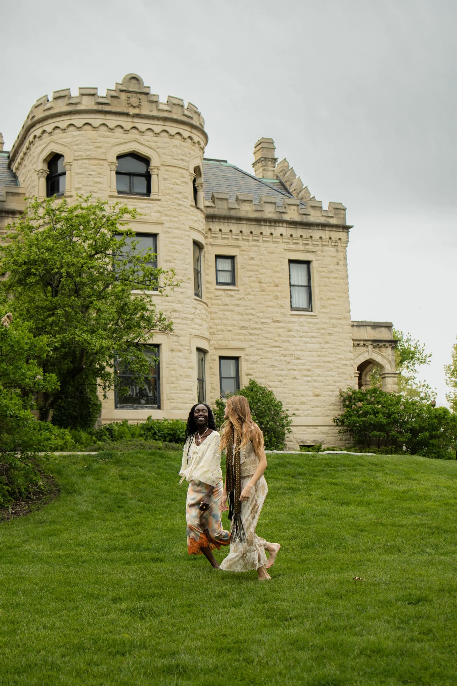 A woman walks across a lawn below a stone castle.