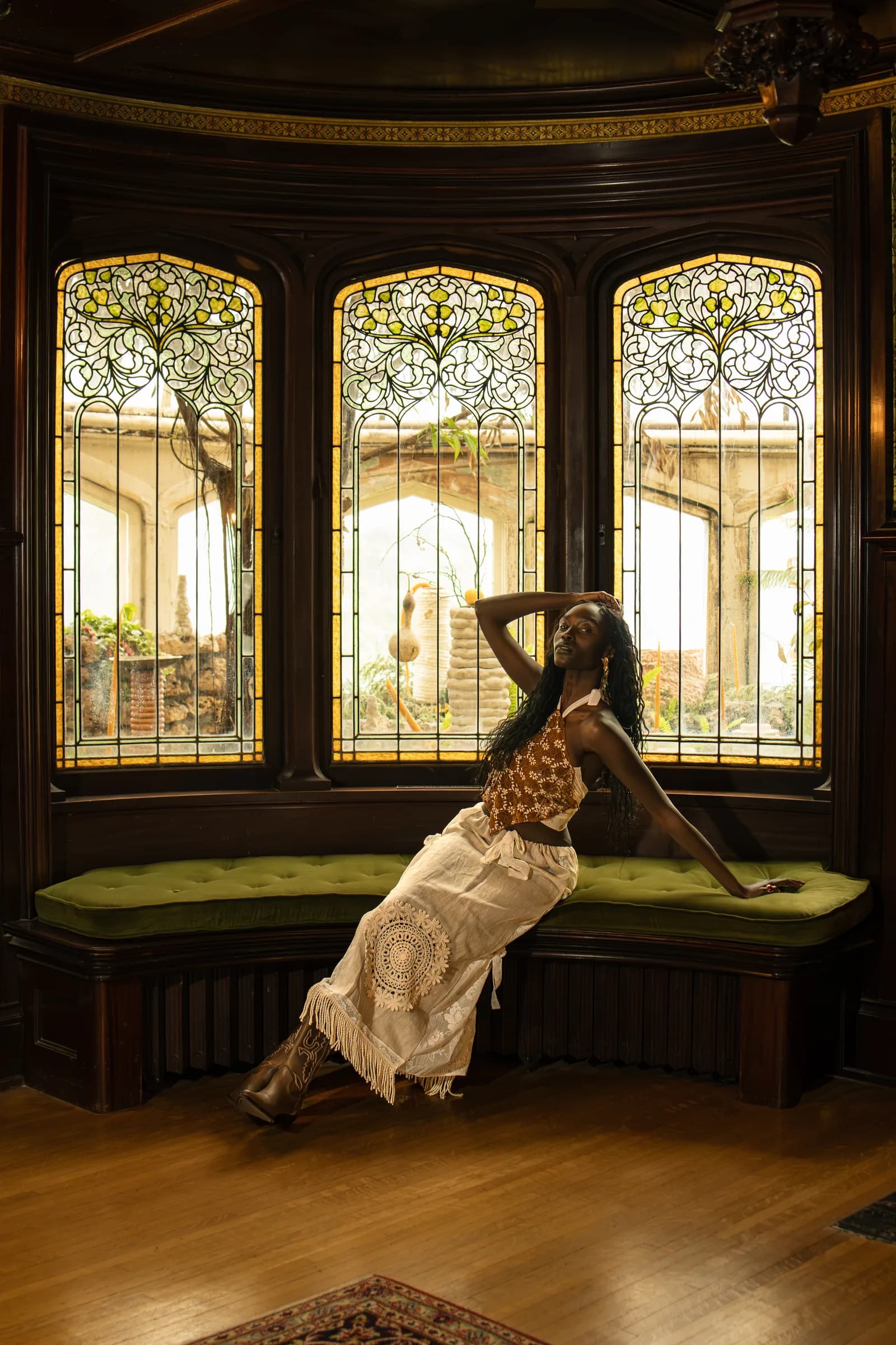 A woman reclines on a green velvet bench below three stained-glass windows.