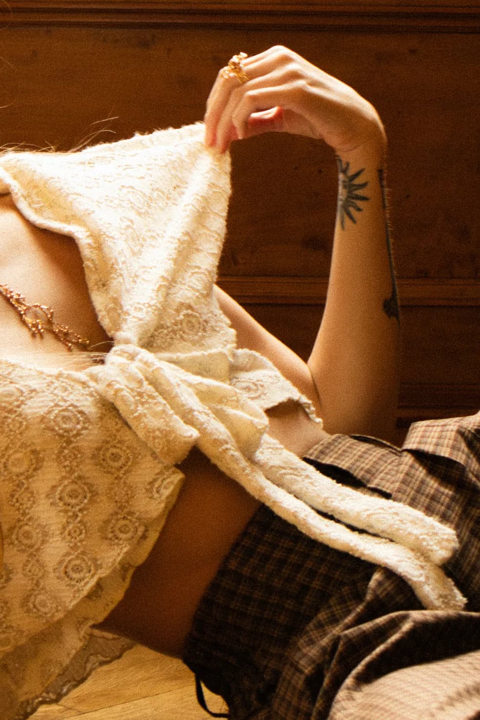 A hand lifts the edge of a cream lace top above a plaid trouser, close up.
