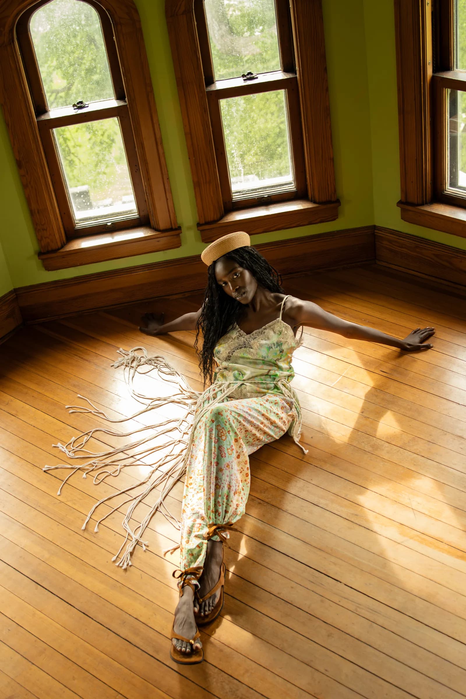 A woman lies on a sunlit wooden floor, the fringe of her trousers fanned out around her.