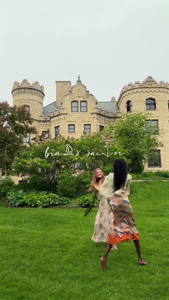 Two women hold hands and spin on the lawn in front of the castle.