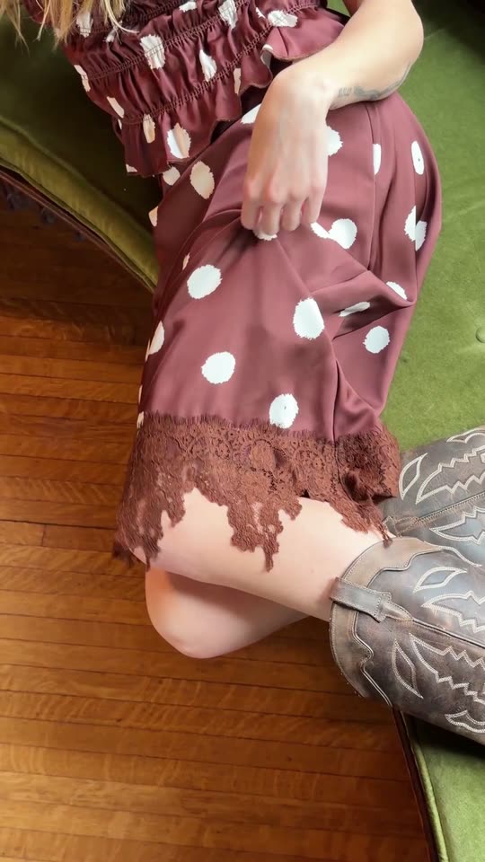 Hands fastening a lace collar and the buttons of a brown shirt, up close.